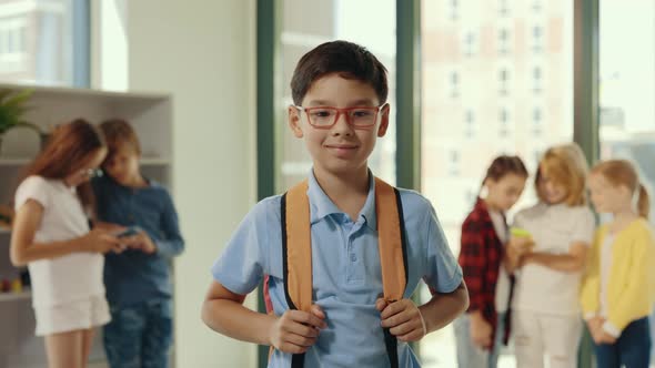 Portrait of the Smiled Asian Pupil Wearing Glasses and Carrying Backpack Standing in the Class While