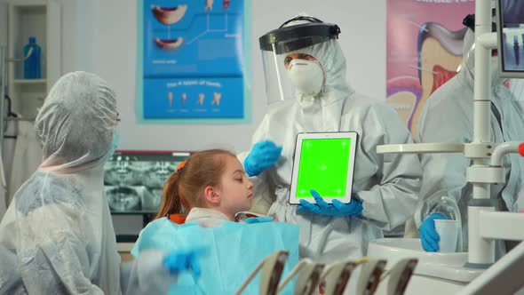 Dentist with Face Shield Pointing at Green Screen Display Talking to Child