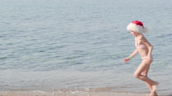 Little Christmas Girl in Santa Claus Hat Running at Ocean Sandy Beach