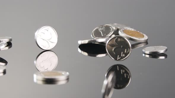 New Israeli Shekels coins falling in slow motion on a reflective surface