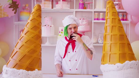 Young Happy Man Dressed As Chef with Dreadlocks Eating Muffin in Bright Confectionery