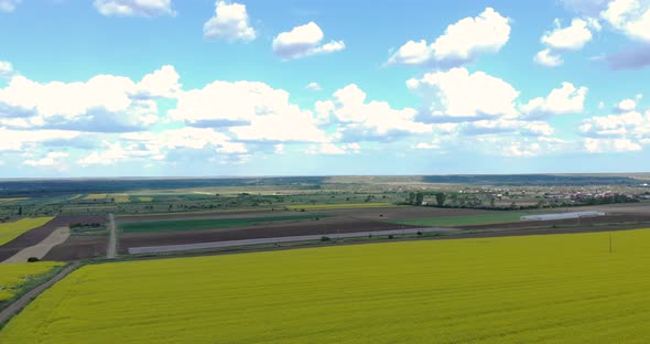 Picturesque View Of A Countryside With Village And Canola Farmland Against Blue Cloudy Sky. - Aerial