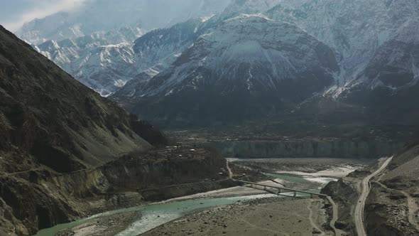 Cinematic Aerial View Of Hunza Valley River With Tilt Up Reveal Of Snow Capped Mountains. Dolly Forw