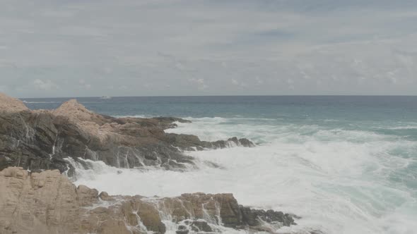 Zoom out view of a jagged rocks being hit by the waves