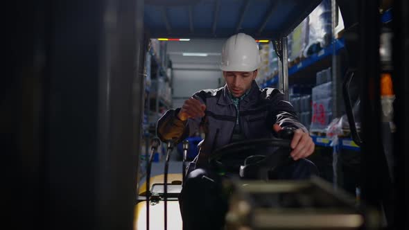 Tired Young Handsome Forklift Driver Taking Off White Hard Hat Wiping Forehead Sitting in Vehicle in