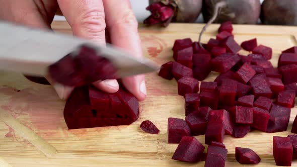 Slicing Purple Raw Beet Into Small Cubes for Vegetable Soup or Salad on Wooden Cutting Board