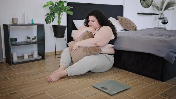 Young Plussize Brunette Looks at Floor Scales Holds Pillow
