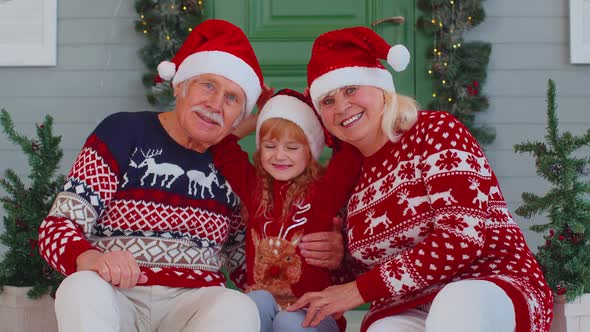 Elderly Grandmother Grandfather with Granddaughter Sitting at Christmas House Porch Waving Hello Hi