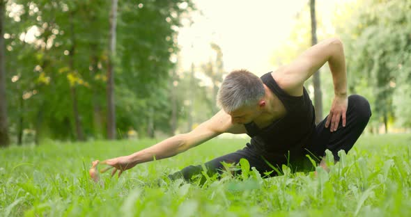 Sporty Man Doing Yoga Moves and Positions on Green Grass