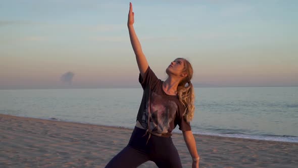 Yoga instructor doing warrior pose on a beach, during sunset with waves flowing in the background.