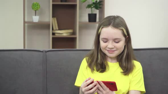 The Little Girl is Smiling and Looking at Her Phone While Sitting on the Couch