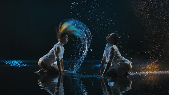 Two Adult Sexy Women Create Splashes of Hair While Sitting on the Water Surface in the Studio