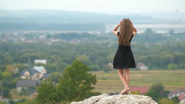 Young Pretty Woman with Long Hair in Black Short Dress Standing Outdoors Enjoying View of Summer