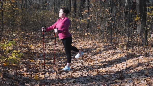 Young cute overweight woman with nordic walking poles stretching before intense training