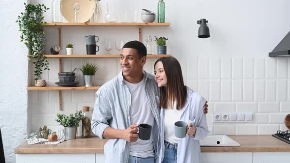 Happy Multiracial Romantic Couple Newlyweds Stylishly Dressed Stand Hugging at Home in the Kitchen