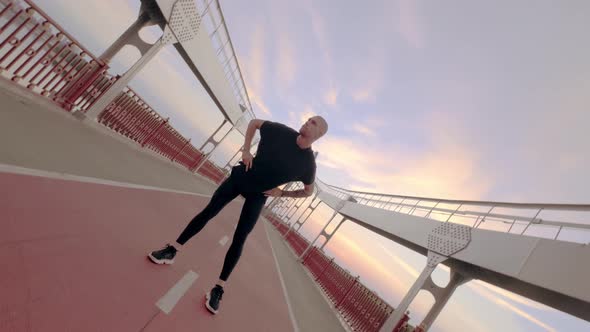 Young White Man in Black Sport Uniform Doing Warmup Before Run Pedestrian Bridge at Dawn