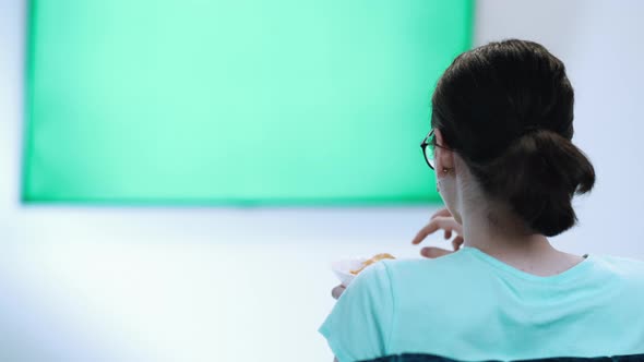 Girl Sits in Font of a Geen Sreen TV Eats Chips and Switches Channels Green Chroma Key Screen TV