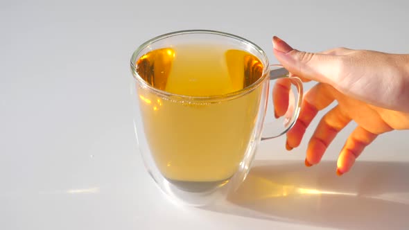 Woman Hand Take Cup of Tea From White Table Herbal Tea in Transparent Glass Mug