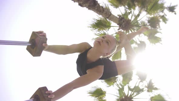 Young Blonde Woman Standing on the Small High Beams with Her Hands in Gymnastic Posture