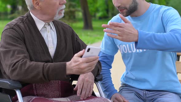 Smiling Male Volunteer Explaining Old Disabled Man How to Use Phone App, Care