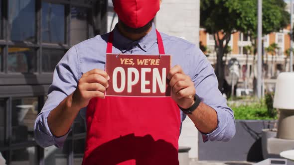 Mixed race male cafe worker wearing face mask showing were open signage