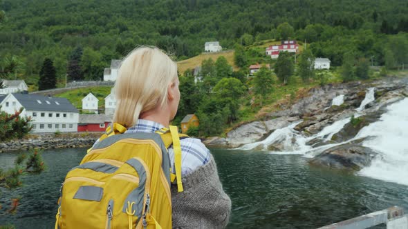 A Woman Admires the Norwegian Village and the Waterfall