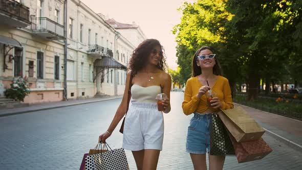 Young Women in Casual Outfit are Holding Colorful Paper Bags and Drinking Cold Tea Laughing and