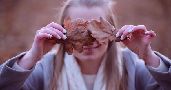 Smiling Woman Hiding Eyes with Leaves in Autumn