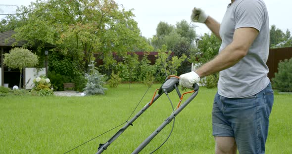 Young Man Works with Lawn Mower in Garden on Spring Day