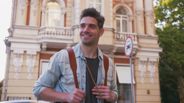 Portrait of Young Smiling Attractive Man Tourist with Backpack in City Center Slow Motion Low Angle