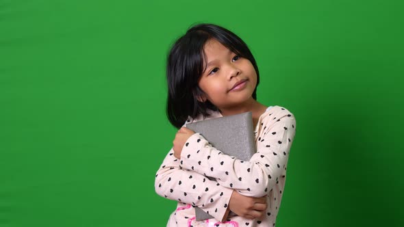 Portrait of cute Asian schoolgirl child 7-8 years looking at camera standing and holding book on the