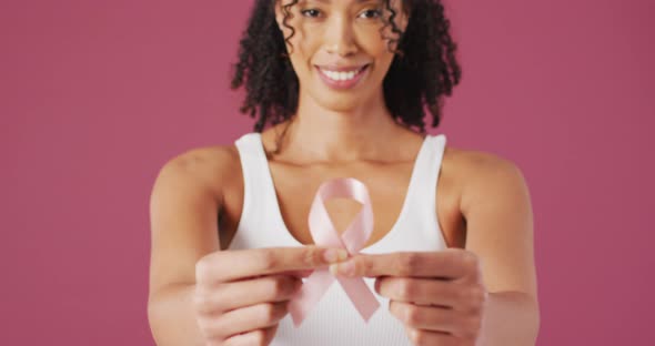 Video of smiling biracial woman holding pink breast cancer ribbon