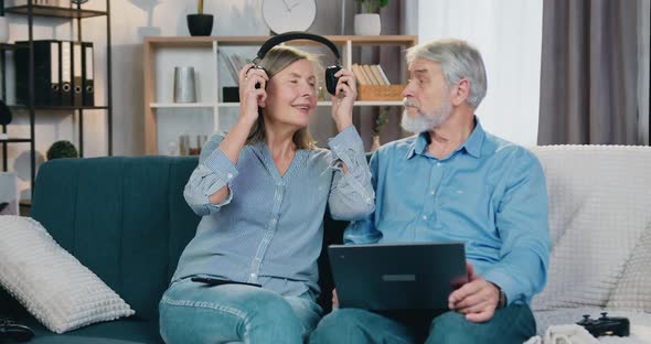 Two Happy Pensioners Using Wireless Laptop and Headphones