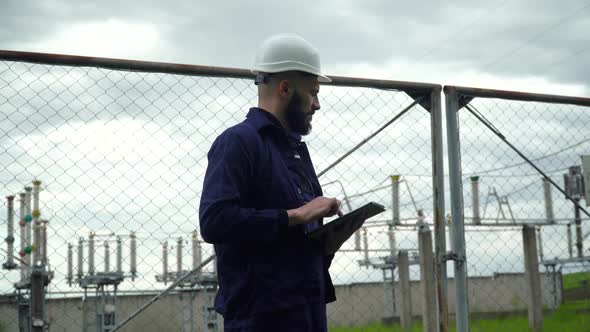 Engineer in Special Uniform Standing with Tablet Near Power Station. Male Monitoring System