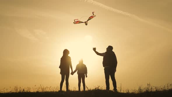 Happy Family Playing with a Kite While on Meadow, Sunset, in Summer Day. Funny Family Time. Happy