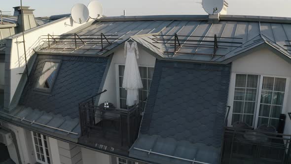 White Wedding Dress Hangs on Special Hanger in Doorway of Balcony of Luxury House Aerial View