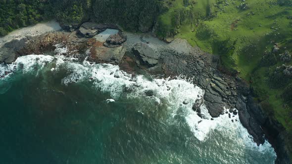 Aerial pan up, black rocky beach, ocean waves crashing into sea foam