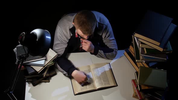 Man Leafing Through the Book and Falls Asleep. Black Background. View From Above