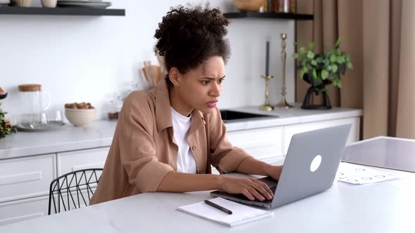 Frustrated Upset African American Brunette Girl Freelancer Manager Sits at the Table in the Kitchen