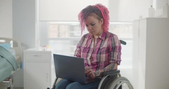 Disabled Woman Sitting in Wheelchair and Using Laptop in Hospital Ward
