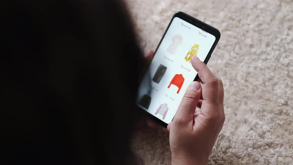 Woman Holding Smartphone Buying Fashion Clothes in Online Store at Cozy Home While Lying on Carpet