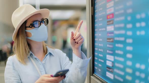 Female Traveler in COVID-19 Face Mask Checking Flight Schedule in Airport 