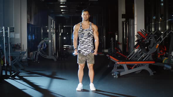 Athletic Handsome Man Works out and Lifts Hands With Dumbbells in Gym