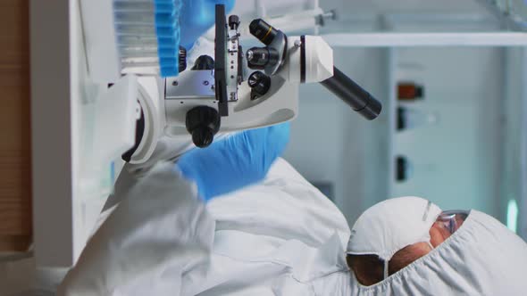 Vertical Video Close Up of Scientist Looking Through a Microscope Wearing Ppe Suit