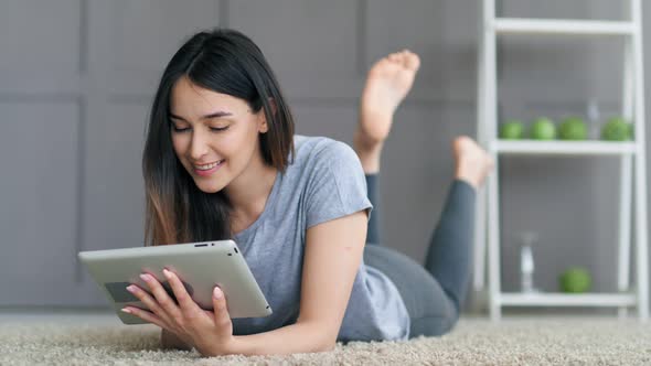 Young Happy Woman Lying on the Floor and Using Tablet Computer at Home