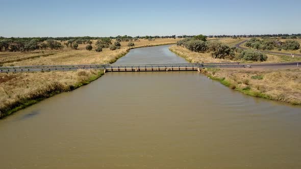 Aerial view of a bridge over a wide, murky river. The camera flies over and past.