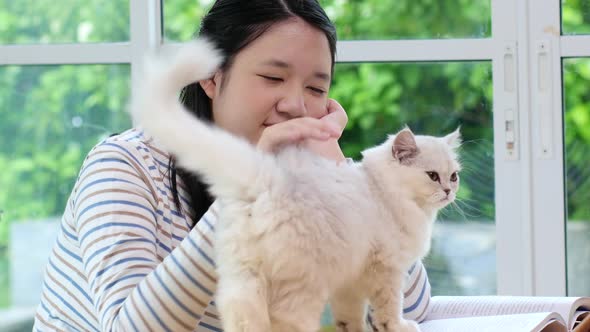 Happy Asian Girl Playing With Pet Cat While Doing Homework