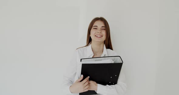 Portrait of Young Happy Girl Looks on Black Folder in Hands and Smiles at Camera