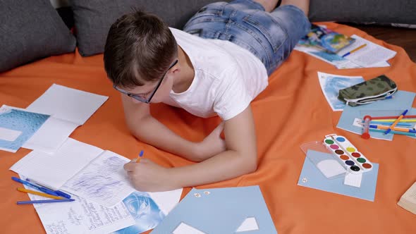 Child Writing with a Pen in a Notebook Lying on an Orange Bedspread in Room