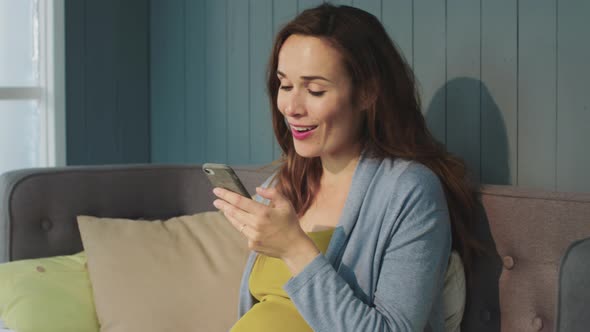 Macro Laugh Pregnant Woman Looking on Smartphone Screen in Modern Living Room